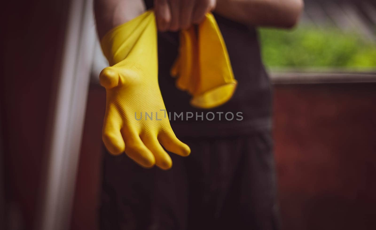 One young Caucasian unrecognizable male builder in black uniform puts on yellow rubber gloves, close-up view from below. The concept of home renovation, construction work.