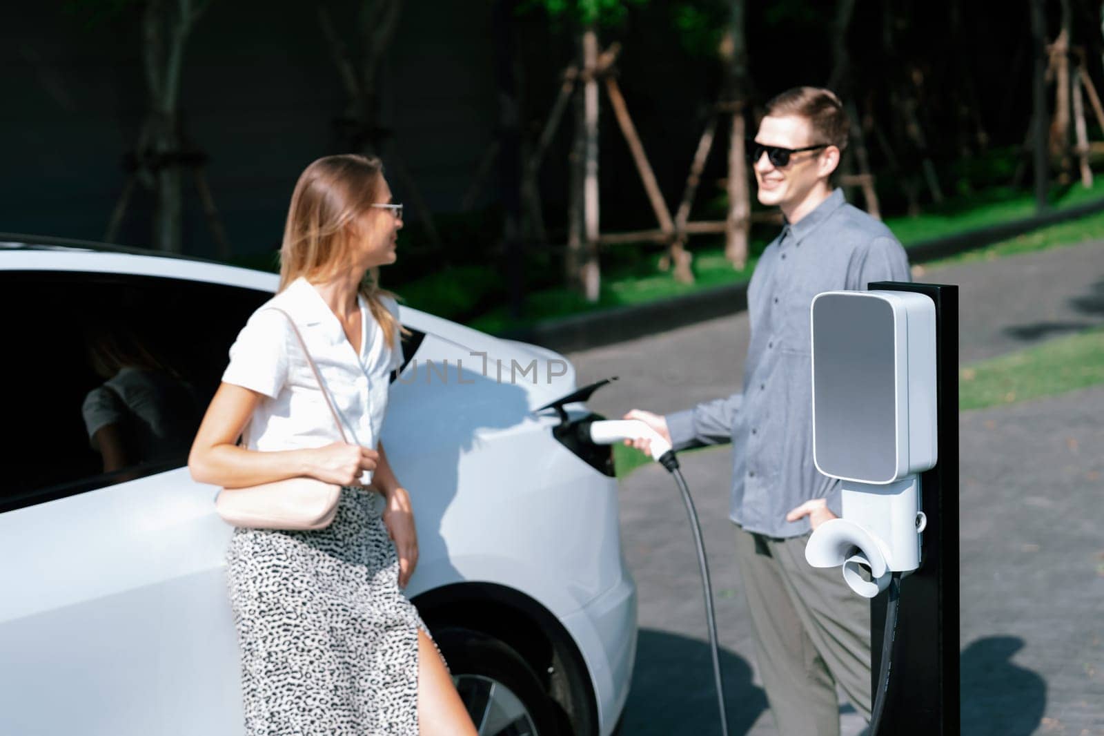 Young couple travel with EV electric car in green sustainable city innards by biancoblue