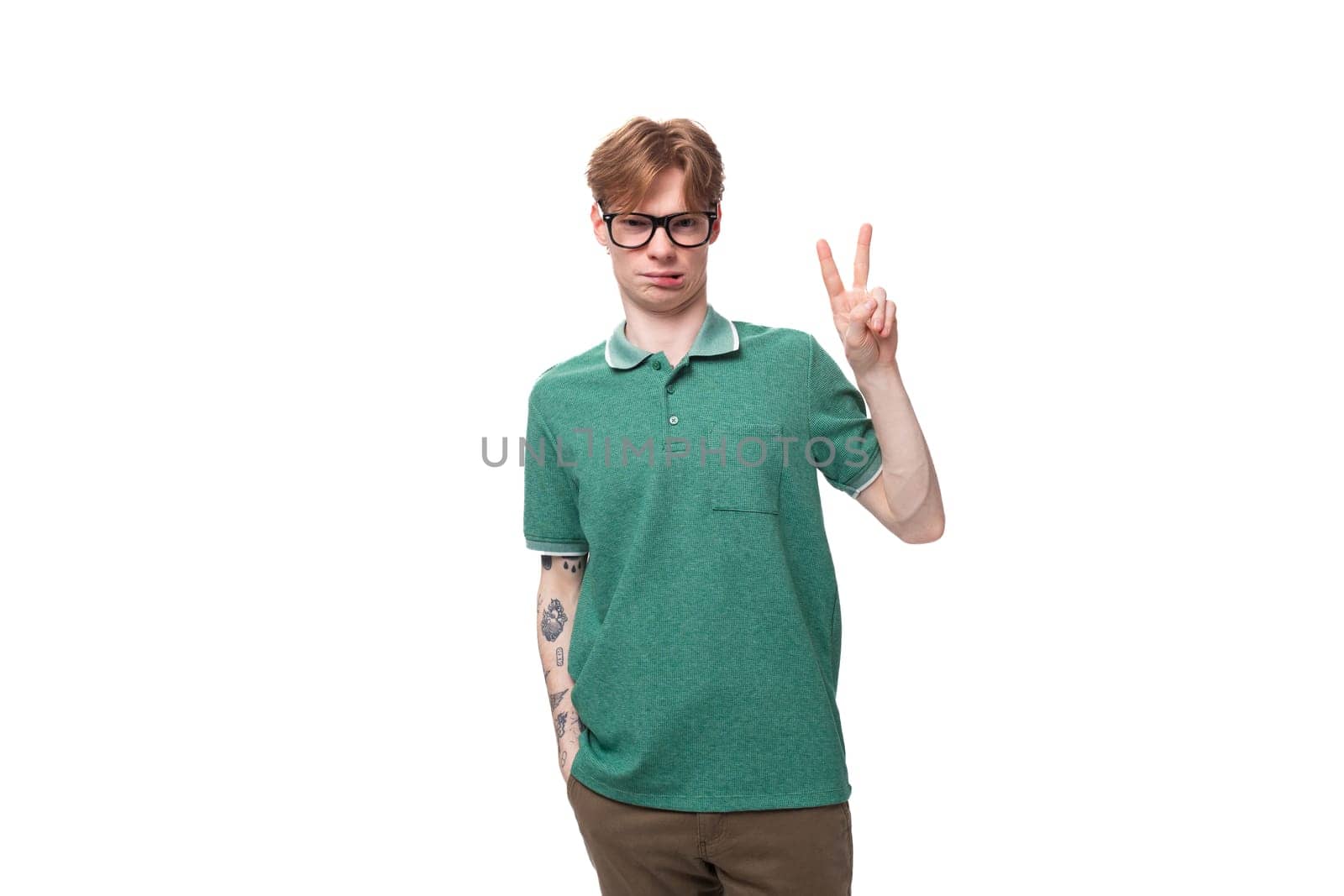 a young european man with red hair and a stylish hairstyle is dressed in a green summer t-shirt shows a greeting with his hand.