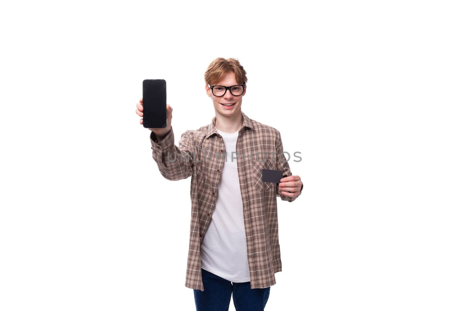 young stylish man with red hair dressed in a summer shirt shows the screen of a vertical smartphone with a mockup by TRMK