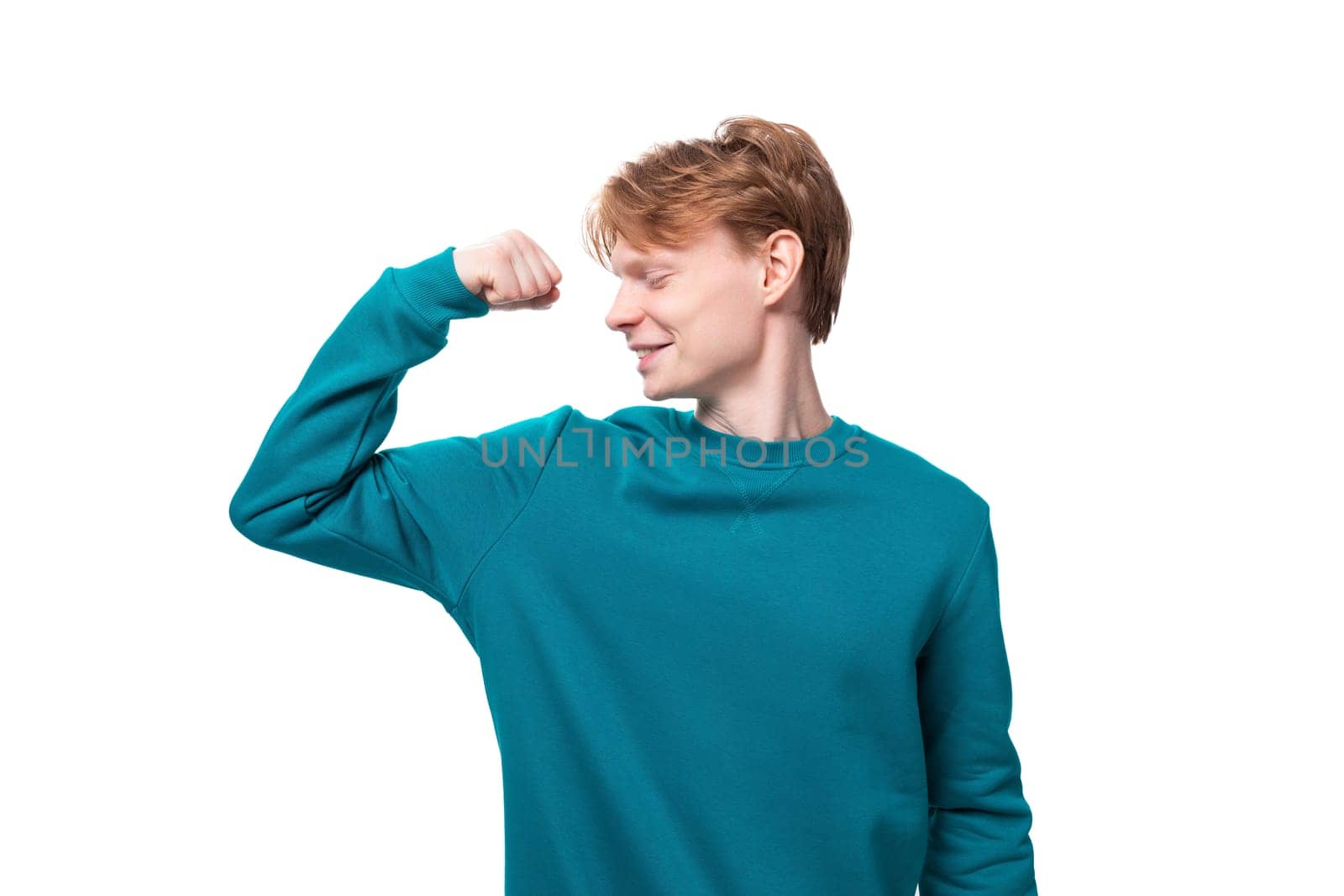 a young guy with red hair dressed in a blue pullover shows strength.