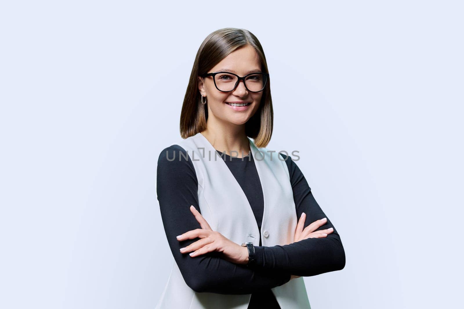 Smiling confident young woman with eyeglasses, crossed arms posing on white studio background. Attractive female in black and white clothes. Beauty fashion style youth business job work staff employee