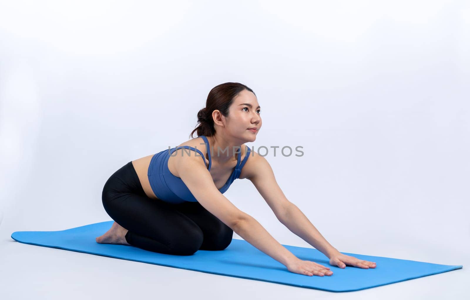 Asian woman in sportswear doing yoga exercise on fitness mat as her workout training routine. Healthy body care and calm meditation in yoga lifestyle in full body shot on isolated background. Vigorous