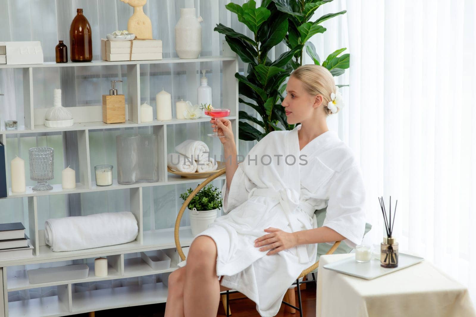 Beauty or body treatment spa salon vacation lifestyle concept with woman wearing bathrobe relaxing with drinks in luxurious hotel spa or resort room. Vacation and leisure relaxation. Quiescent