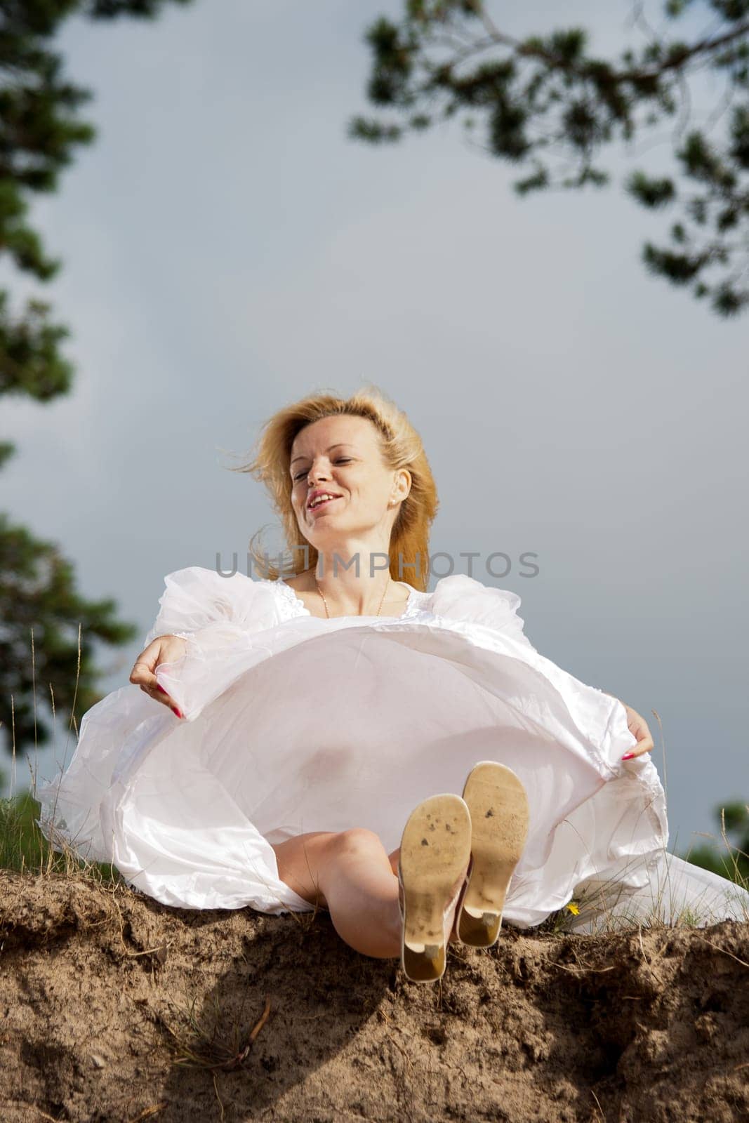 Woman sitting on a cliff in a long white dress and smiling