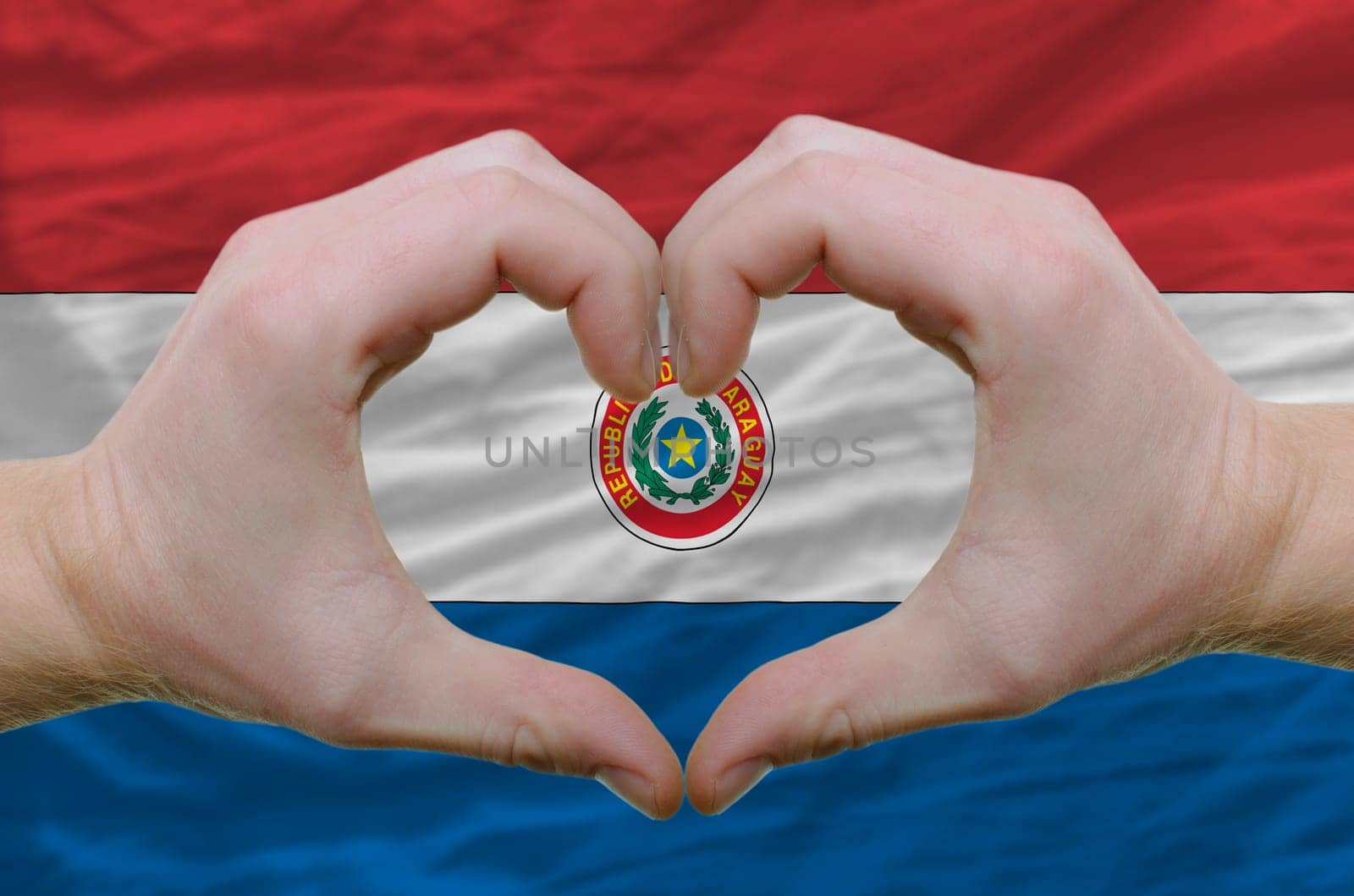 Gesture made by hands showing symbol of heart and love over paraguay flag