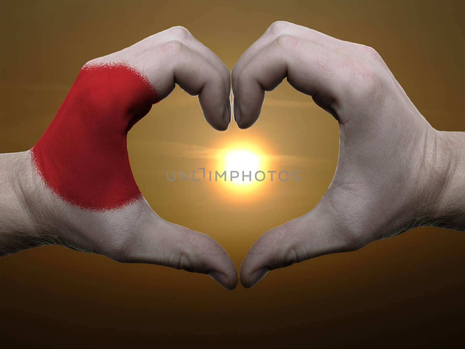 Gesture made by japan flag colored hands showing symbol of heart and love during sunrise