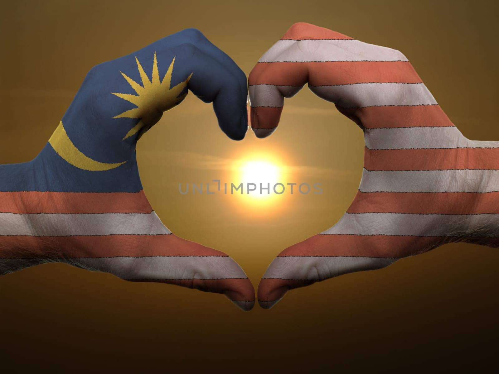 Gesture made by malaysia flag colored hands showing symbol of heart and love during sunrise