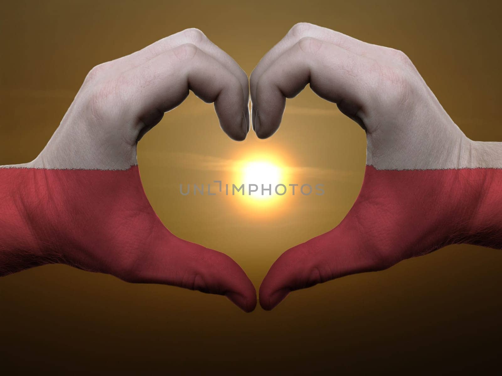 Gesture made by poland flag colored hands showing symbol of heart and love during sunrise