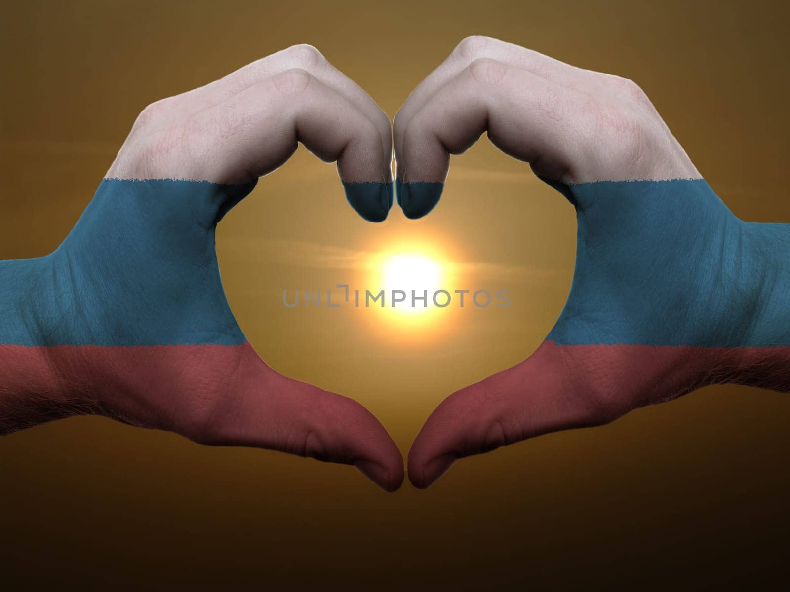 Gesture made by russia flag colored hands showing symbol of heart and love during sunrise