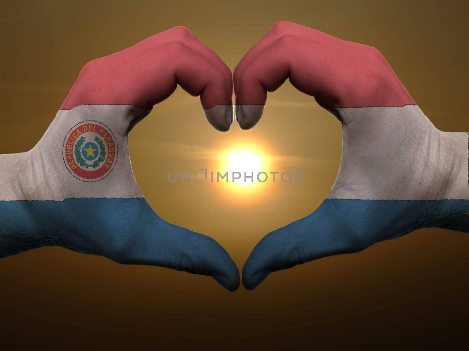 Gesture made by paraguay flag colored hands showing symbol of heart and love during sunrise