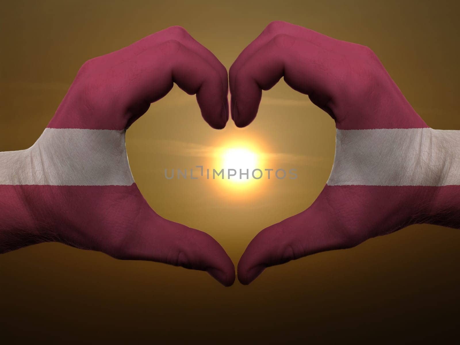 Gesture made by latvia flag colored hands showing symbol of heart and love during sunrise