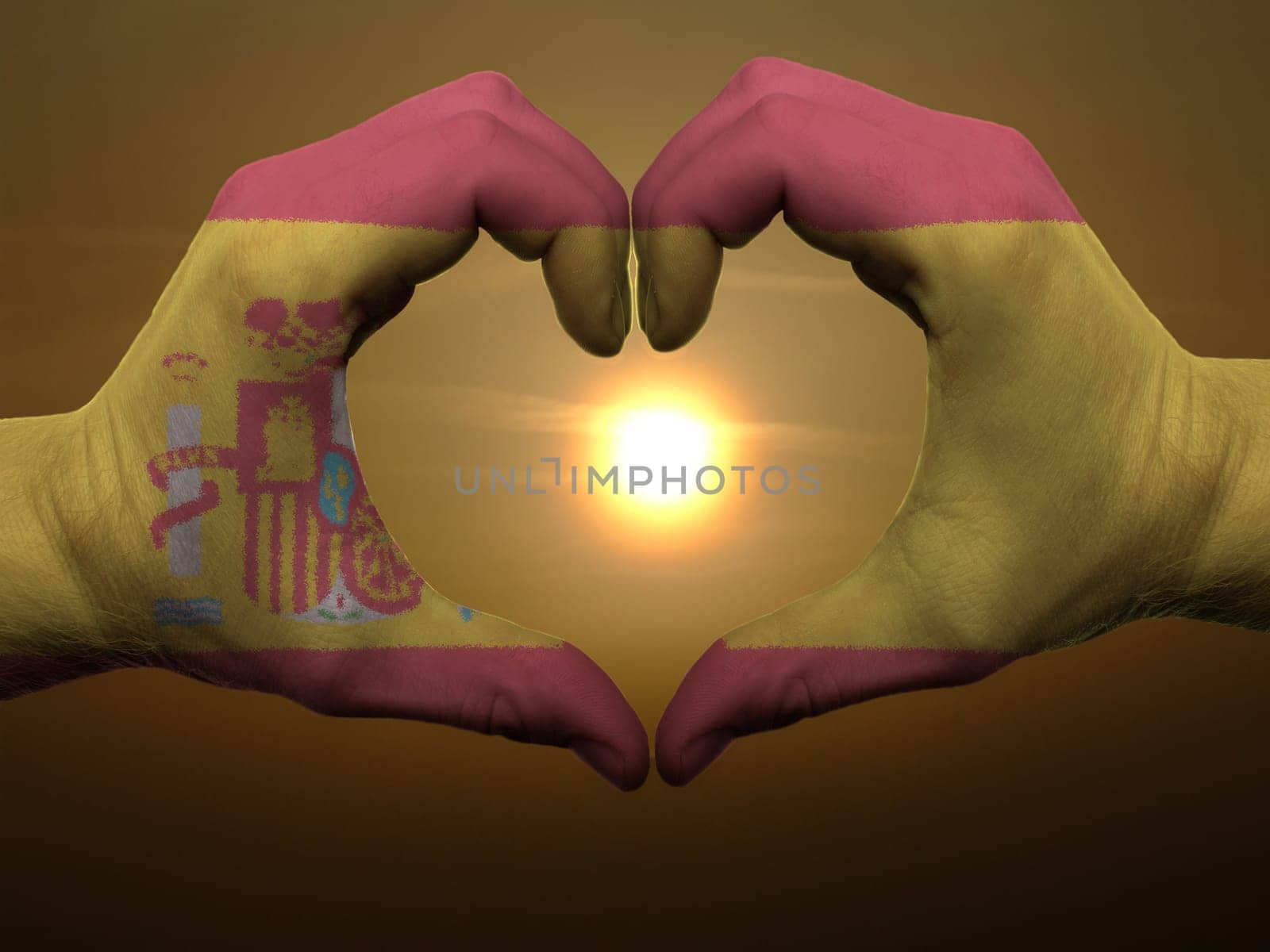 Gesture made by spain flag colored hands showing symbol of heart and love during sunrise