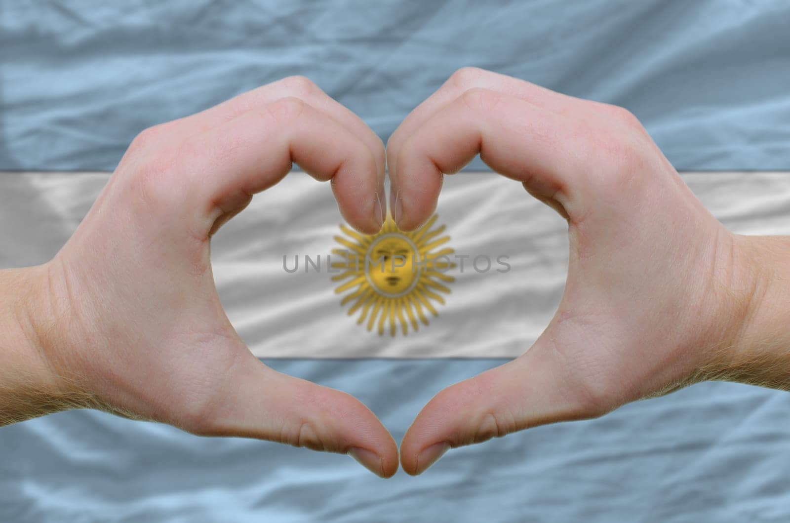 Gesture made by hands showing symbol of heart and love over argentinian flag