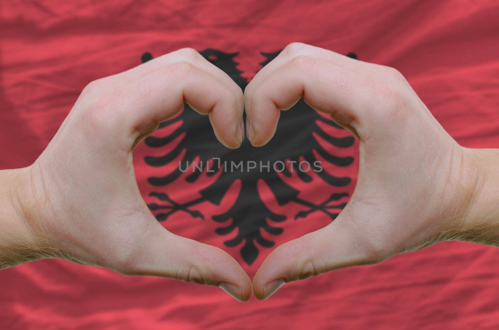 Gesture made by hands showing symbol of heart and love over Albanian flag