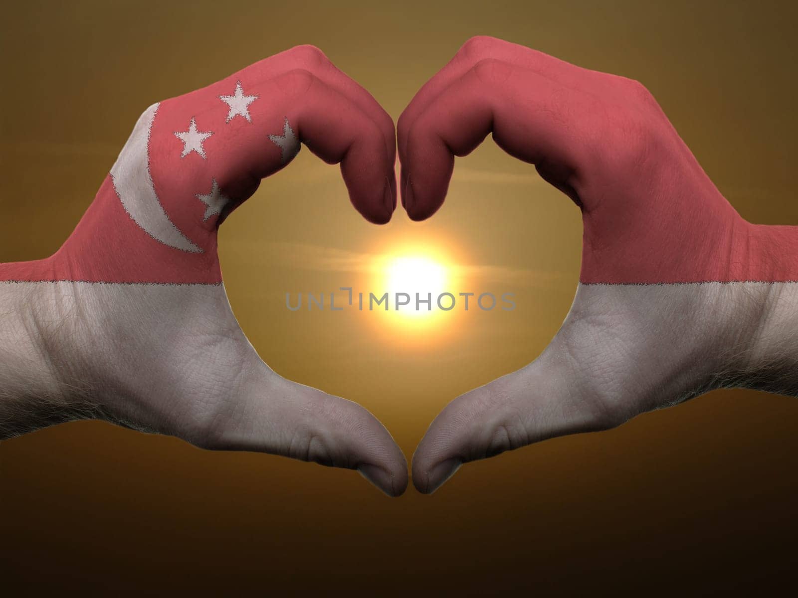 Gesture made by singapore flag colored hands showing symbol of heart and love during sunrise