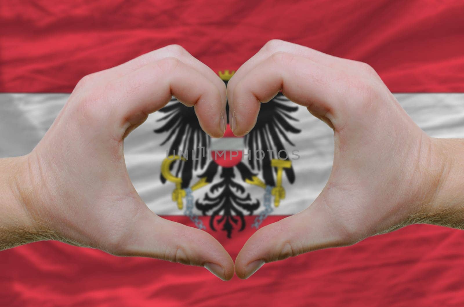 Gesture made by hands showing symbol of heart and love over austrian flag