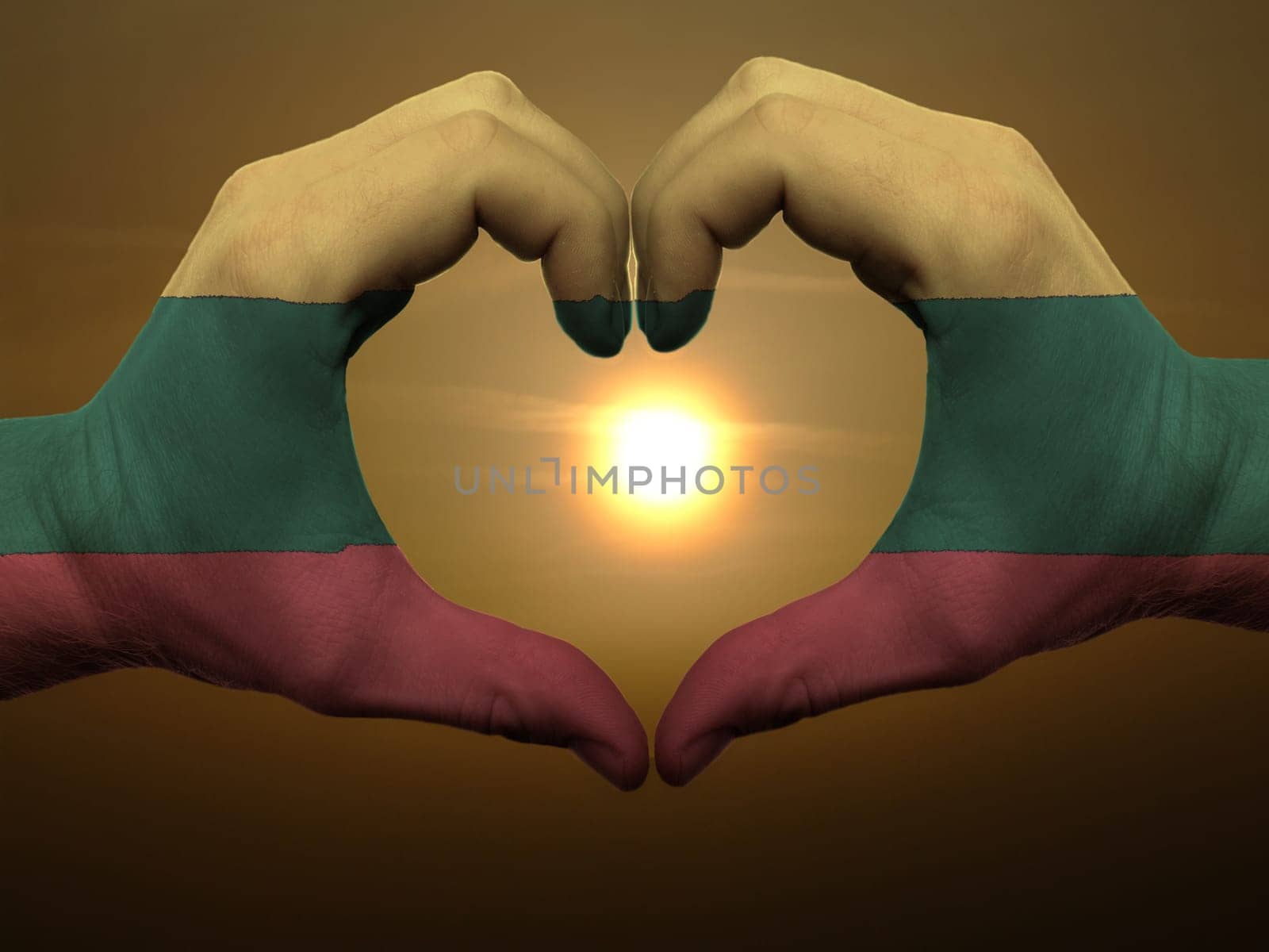 Gesture made by lithuania flag colored hands showing symbol of heart and love during sunrise