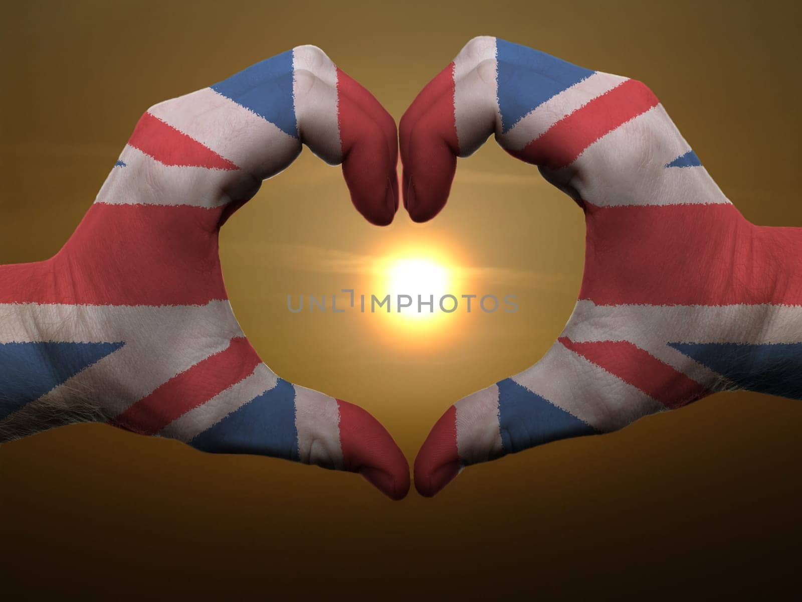 Gesture made by united kingdom flag colored hands showing symbol of heart and love during sunrise