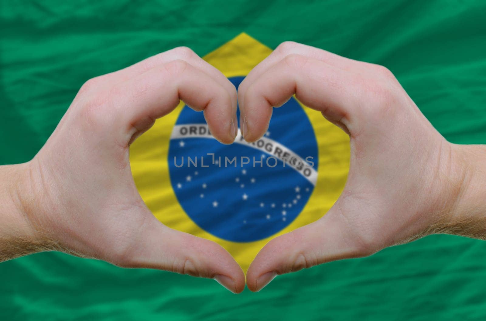 Gesture made by hands showing symbol of heart and love over brazil flag