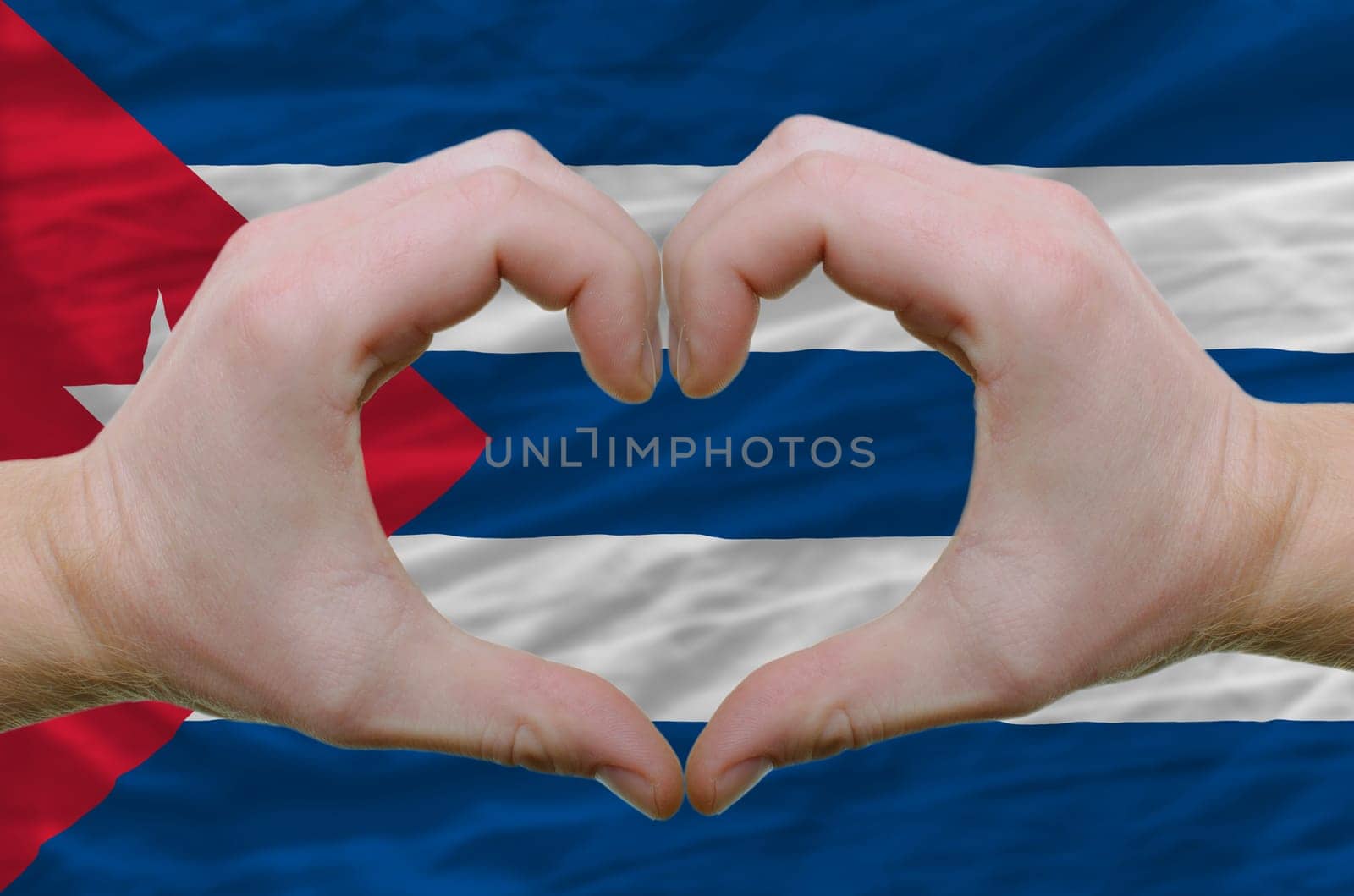 Gesture made by hands showing symbol of heart and love over cuba flag