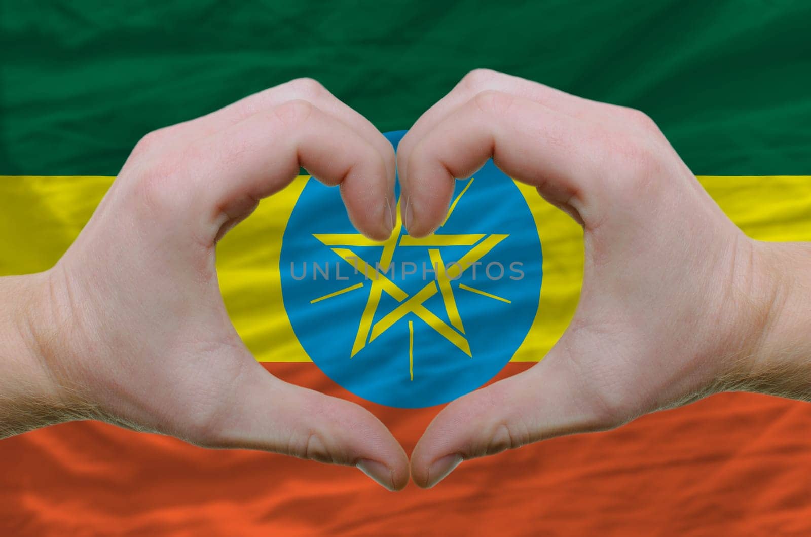 Gesture made by hands showing symbol of heart and love over ethiopia flag