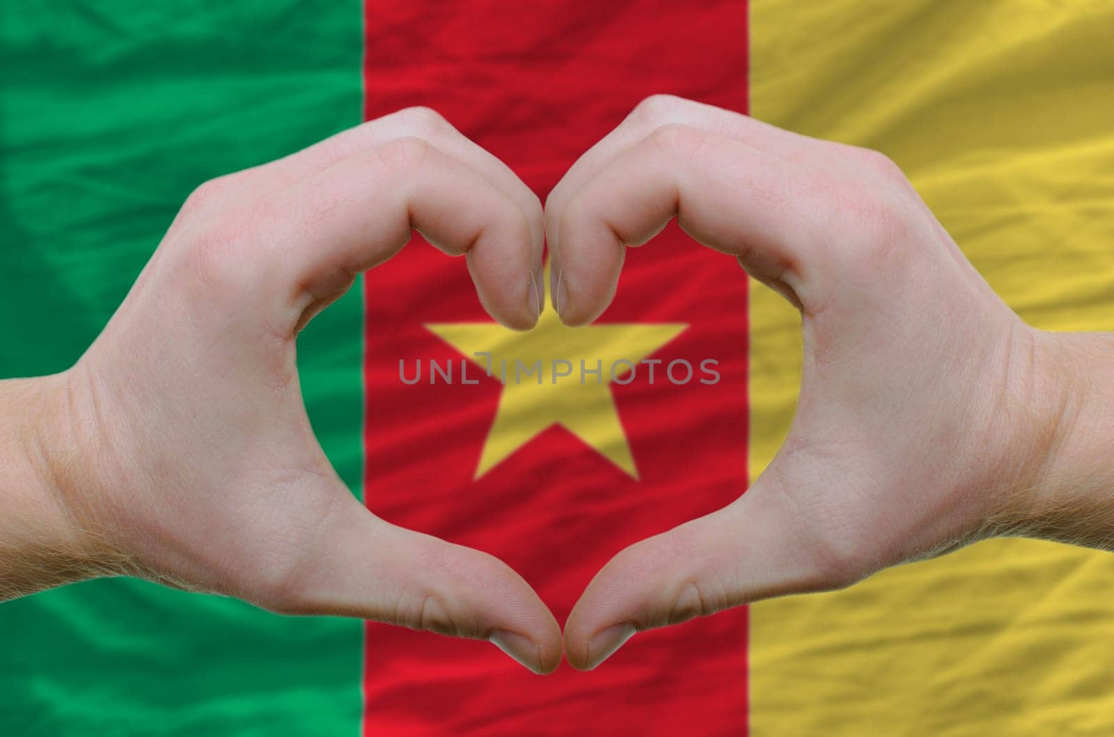 Gesture made by hands showing symbol of heart and love over cameroon flag