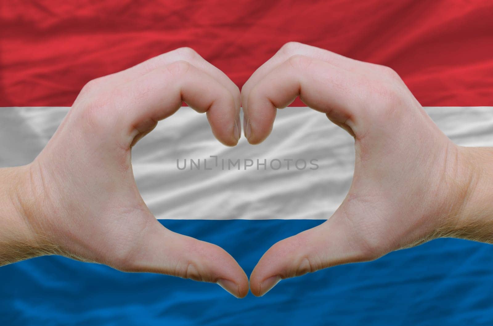 Gesture made by hands showing symbol of heart and love over holland flag