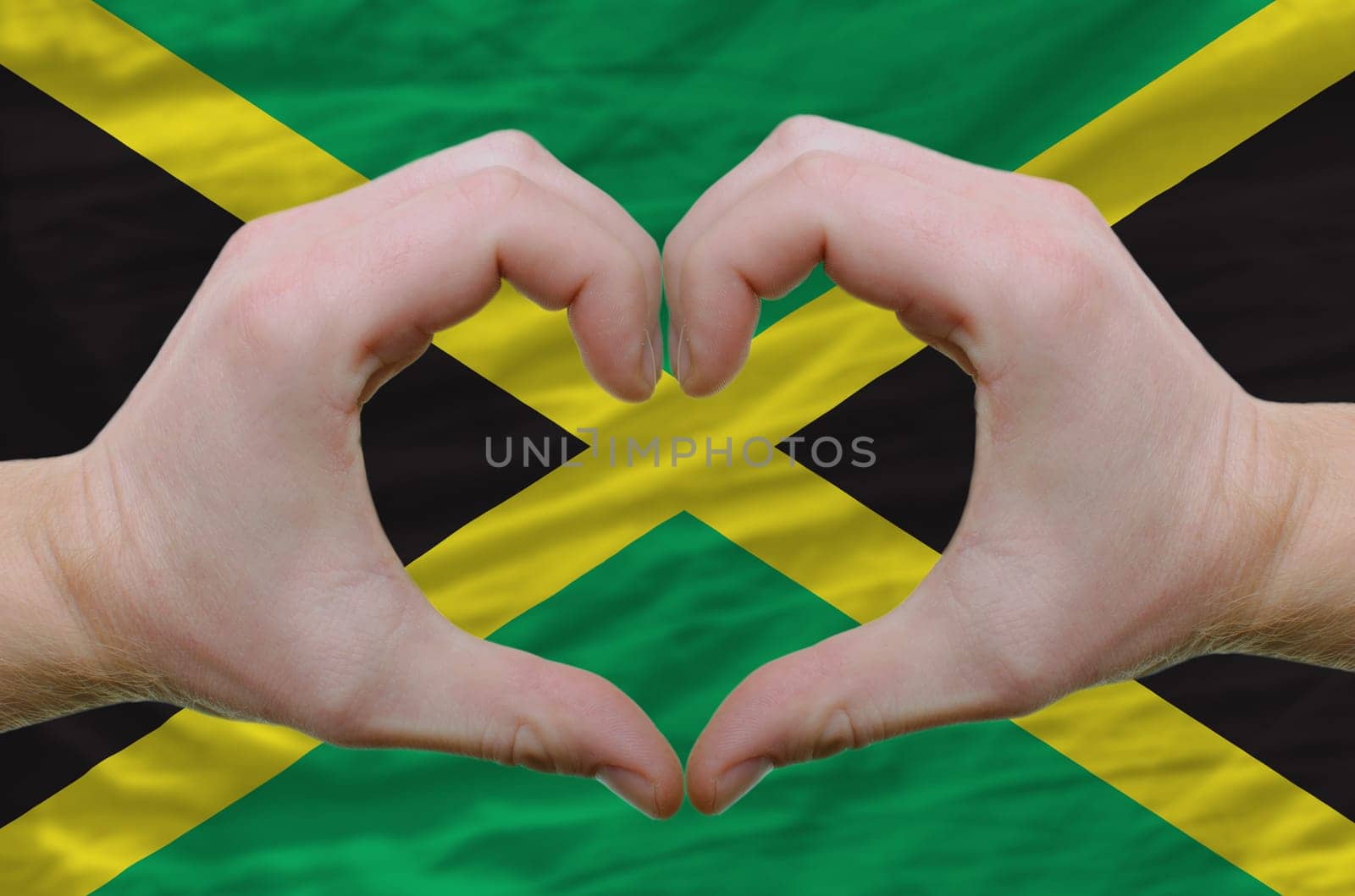 Gesture made by hands showing symbol of heart and love over jamaica flag