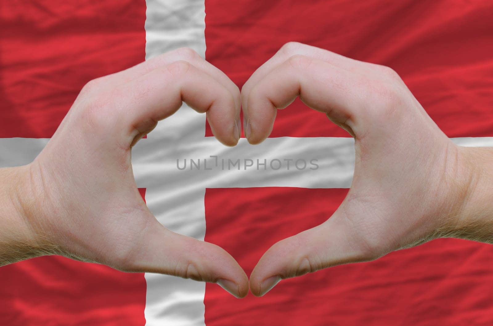 Gesture made by hands showing symbol of heart and love over denmark flag