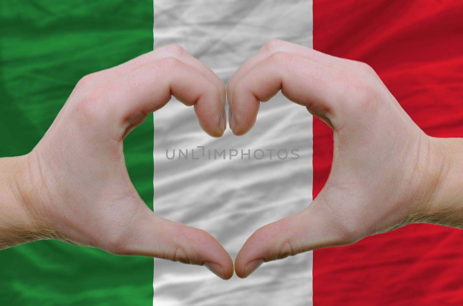 Gesture made by hands showing symbol of heart and love over italy flag