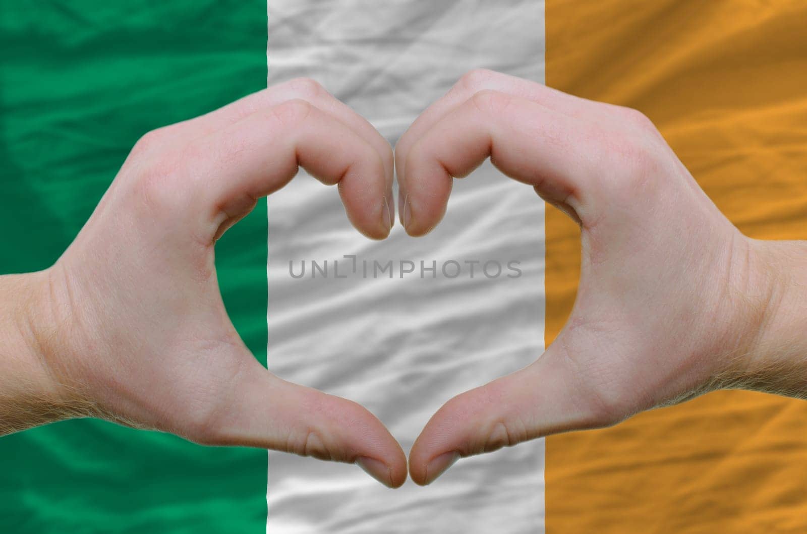 Gesture made by hands showing symbol of heart and love over ireland flag