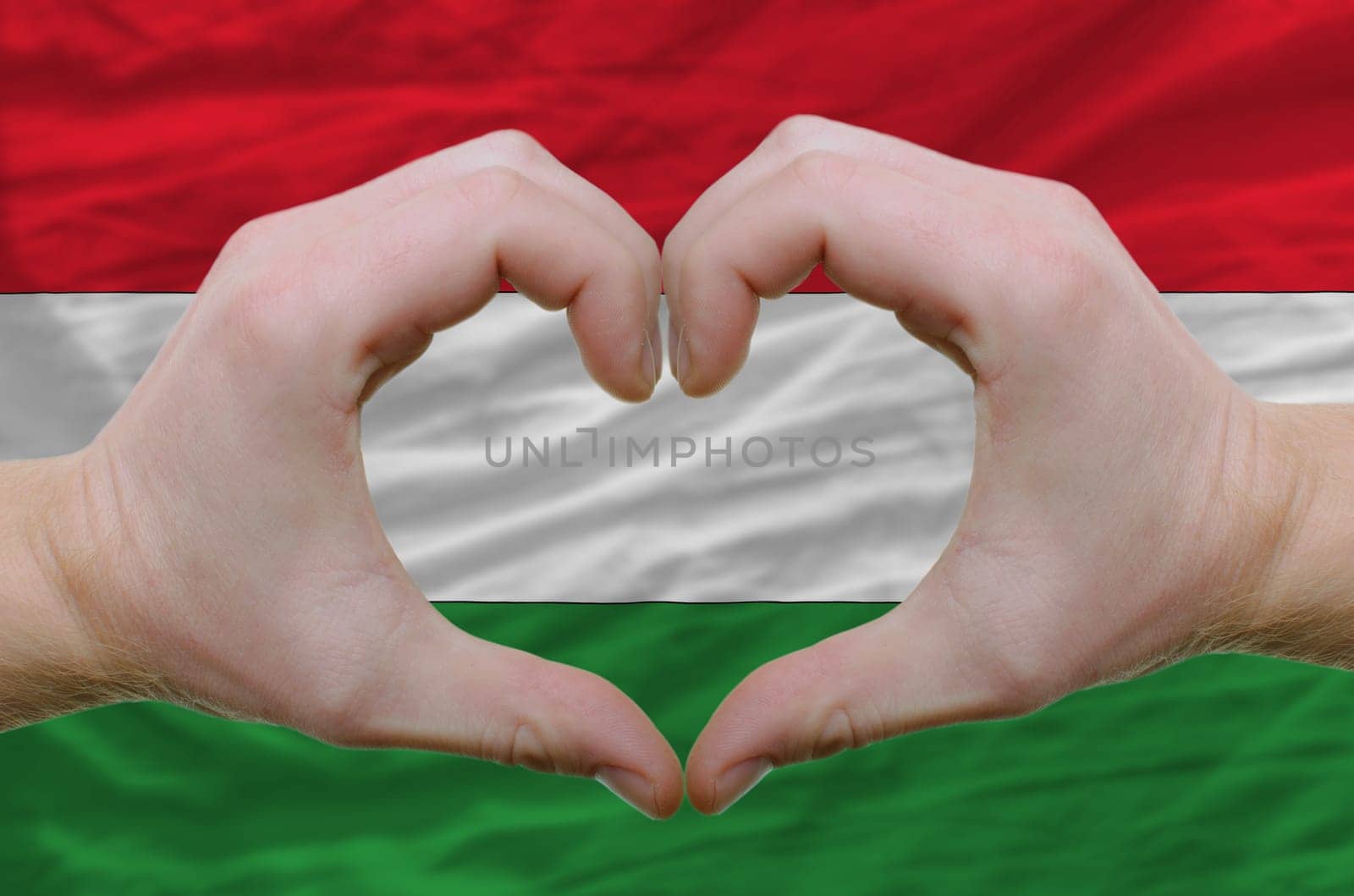 Gesture made by hands showing symbol of heart and love over hungary flag