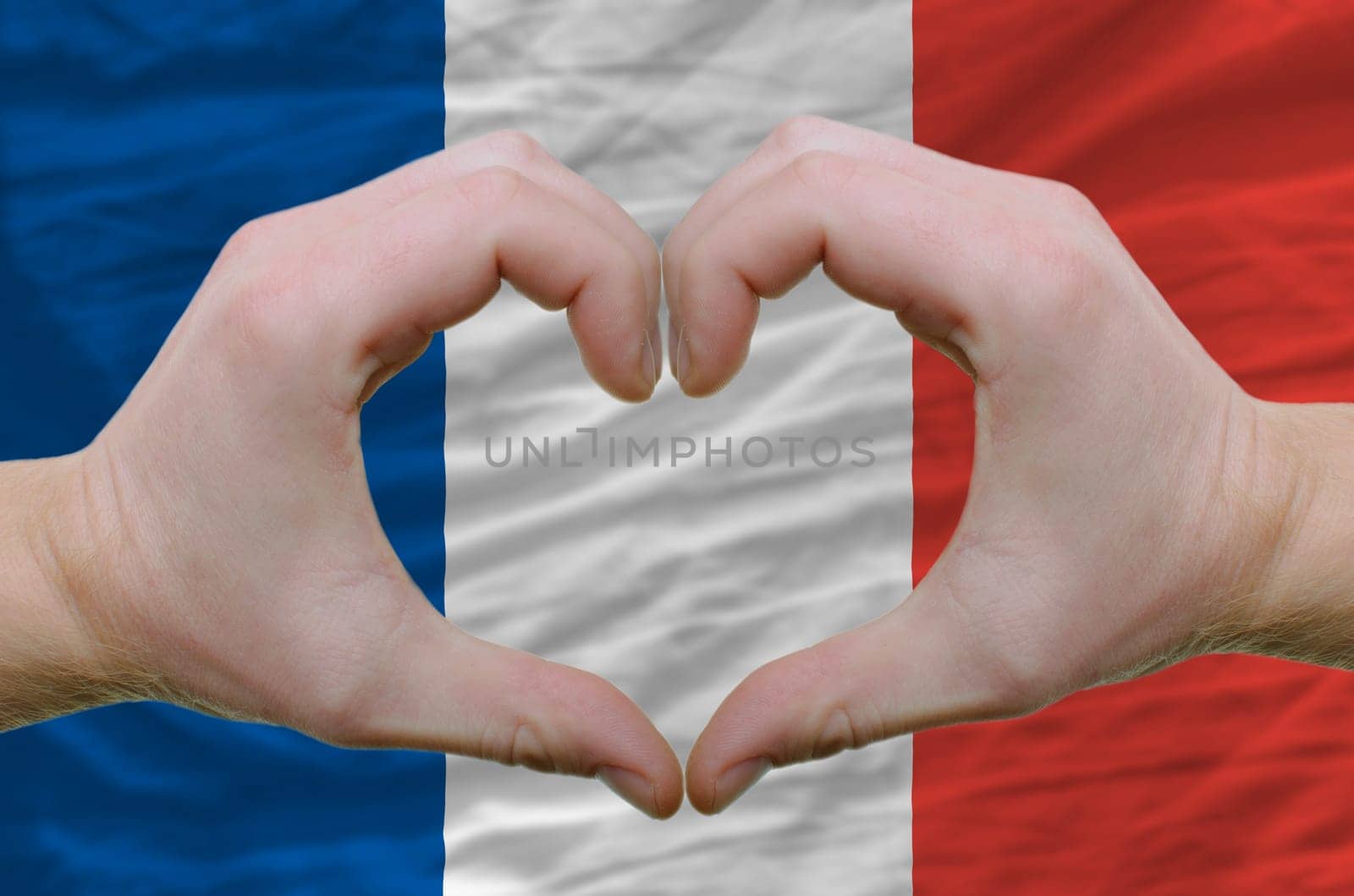 Gesture made by hands showing symbol of heart and love over france flag