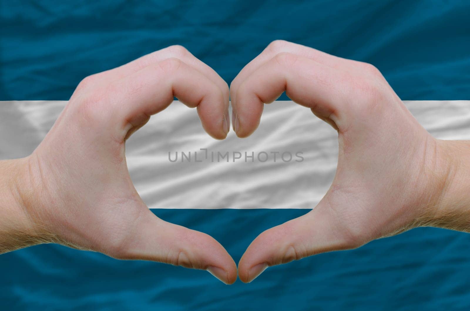 Gesture made by hands showing symbol of heart and love over salvador flag