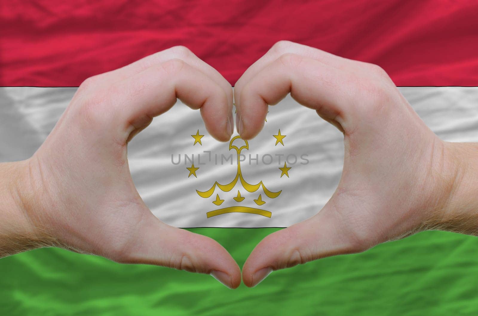 Gesture made by hands showing symbol of heart and love over tajikistan flag