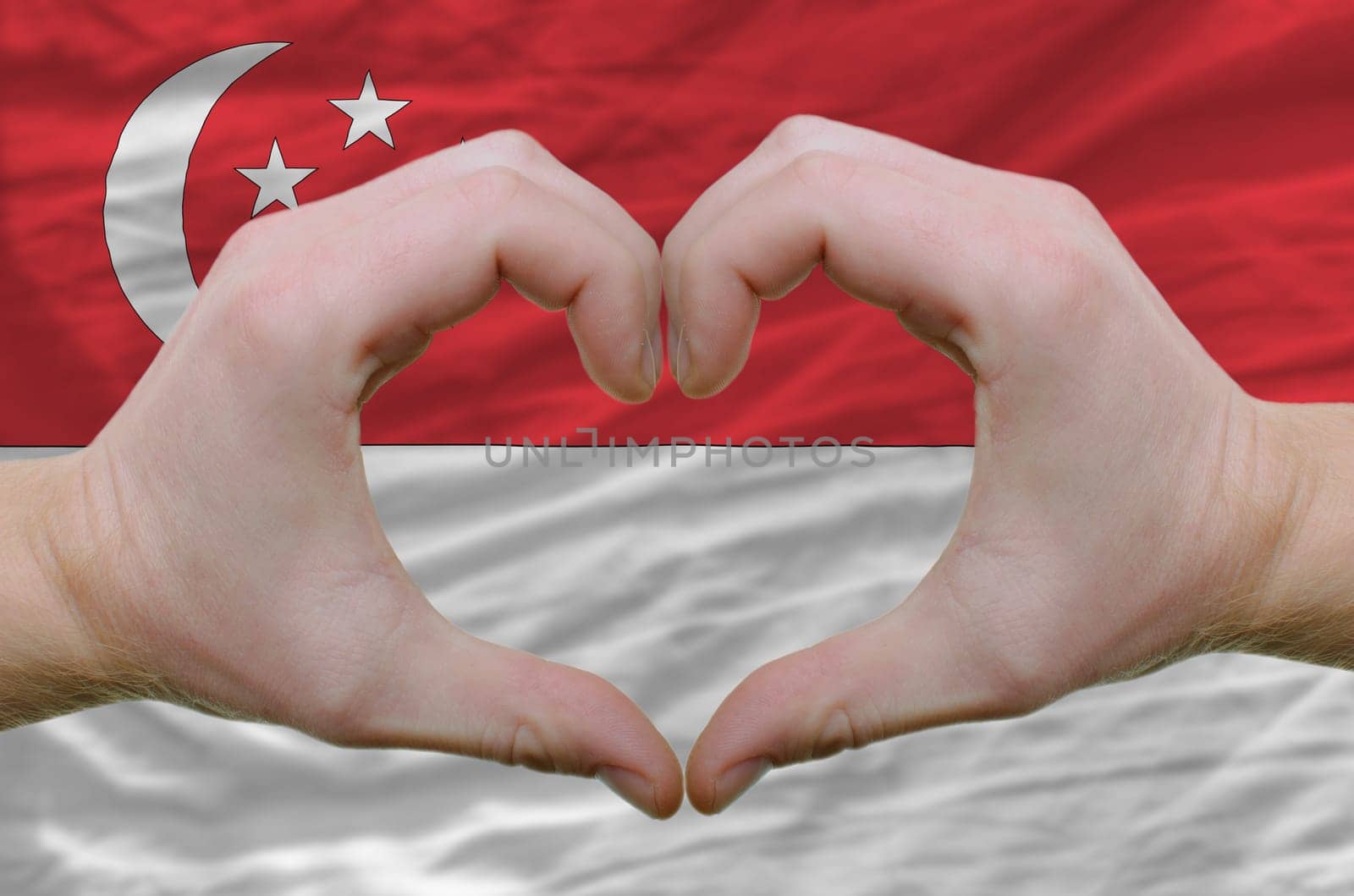 Gesture made by hands showing symbol of heart and love over singapore flag