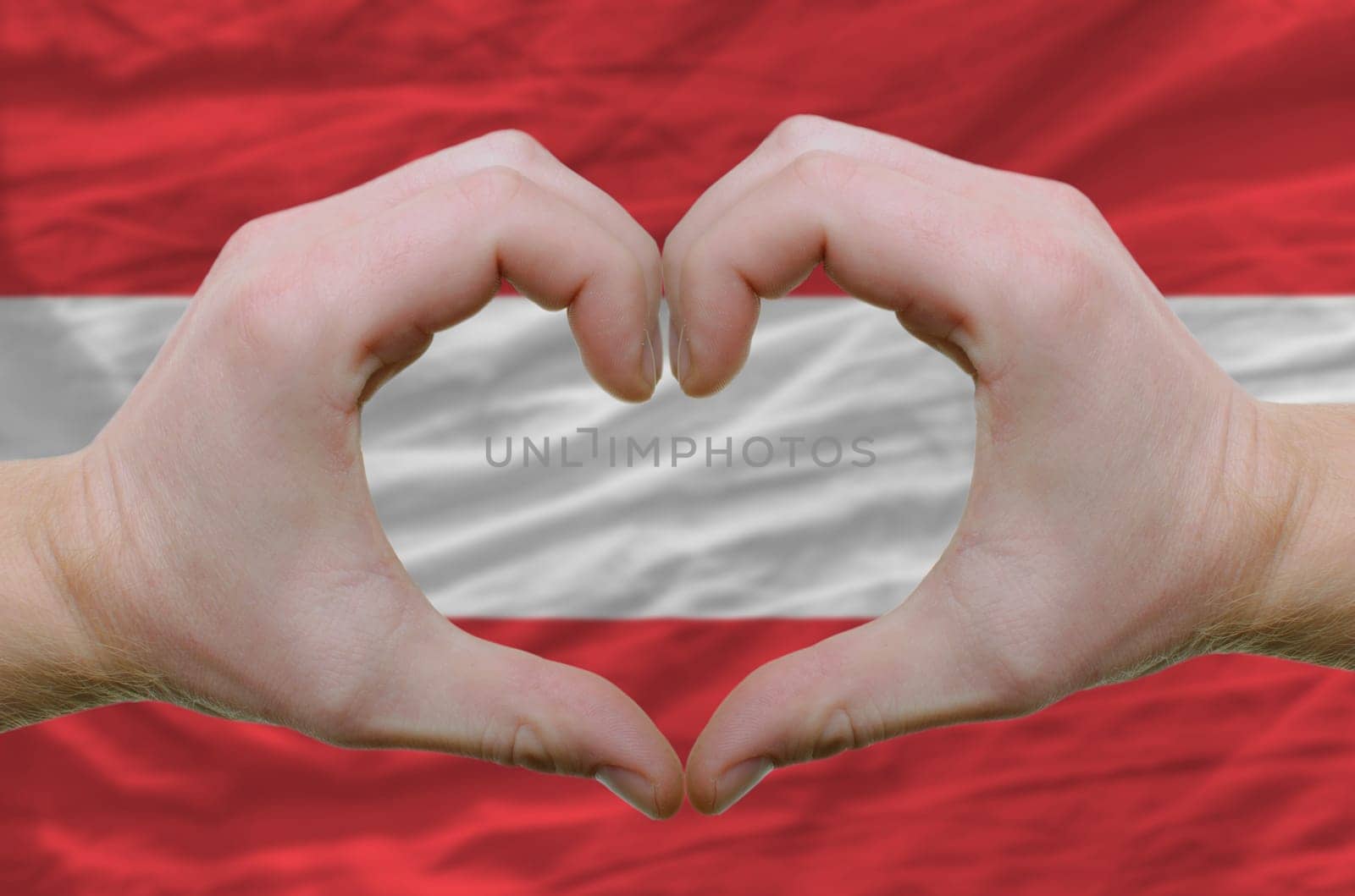 Gesture made by hands showing symbol of heart and love over austrian flag