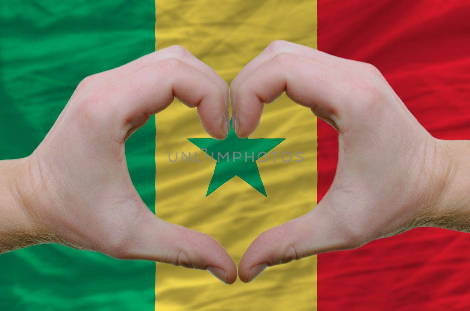 Gesture made by hands showing symbol of heart and love over senegal flag