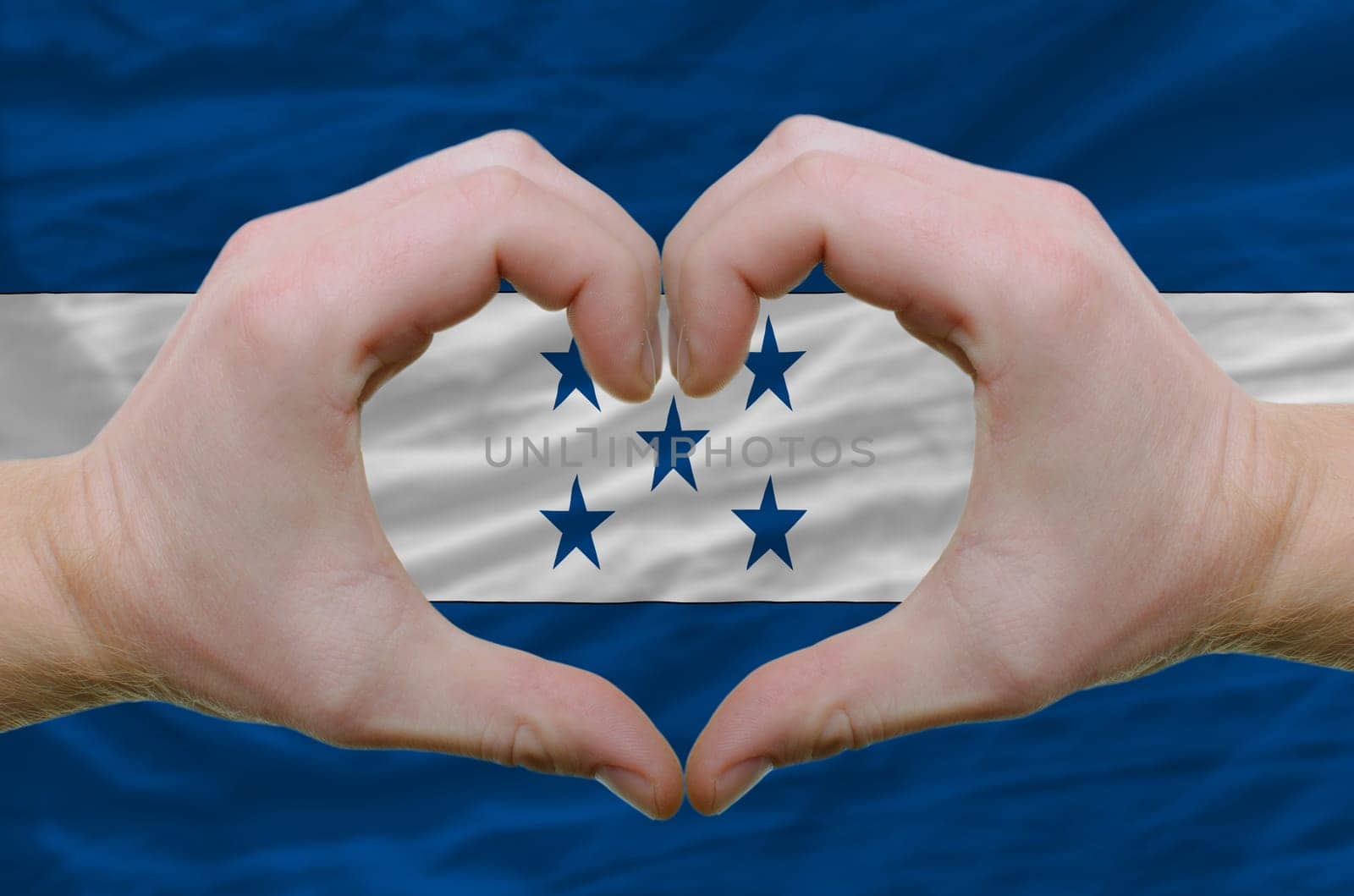 Gesture made by hands showing symbol of heart and love over honduras flag