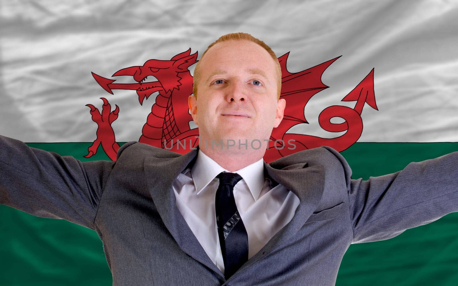 joyful investor spreading arms after good business investment in wales, in front of flag