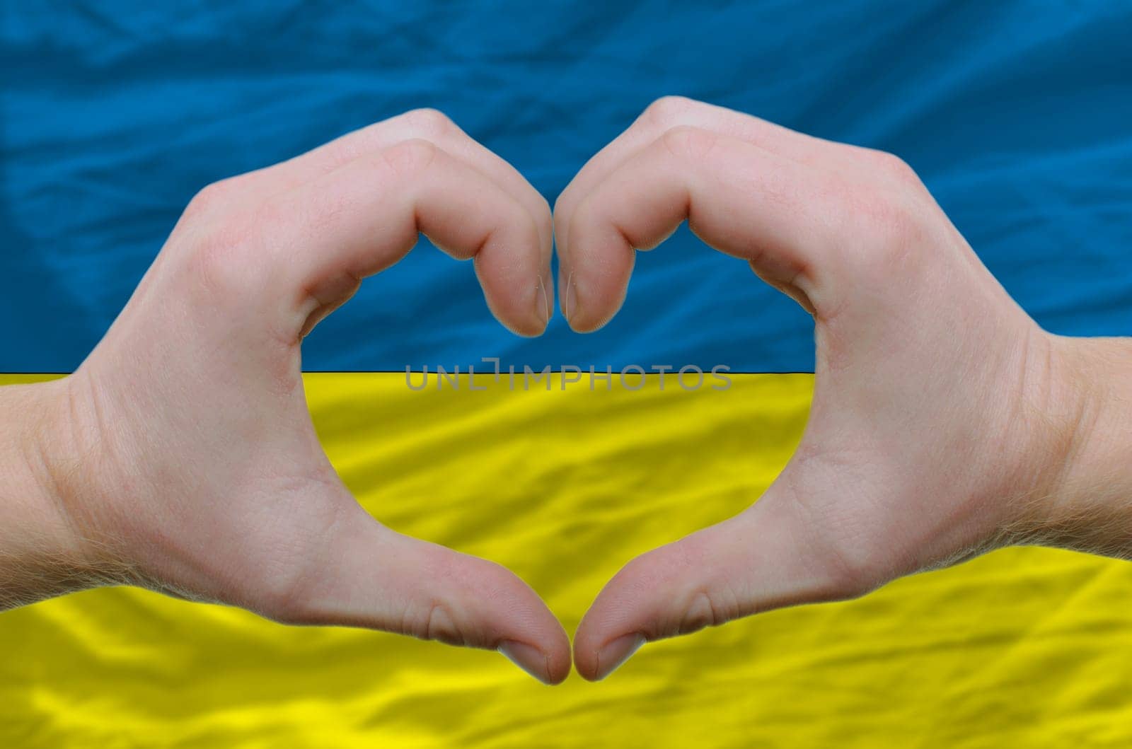 Gesture made by hands showing symbol of heart and love over ukraine flag