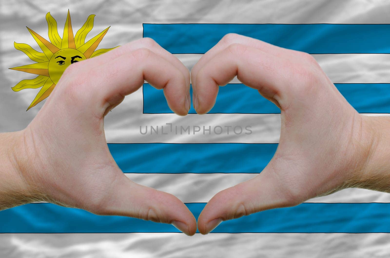 Gesture made by hands showing symbol of heart and love over uruguay flag