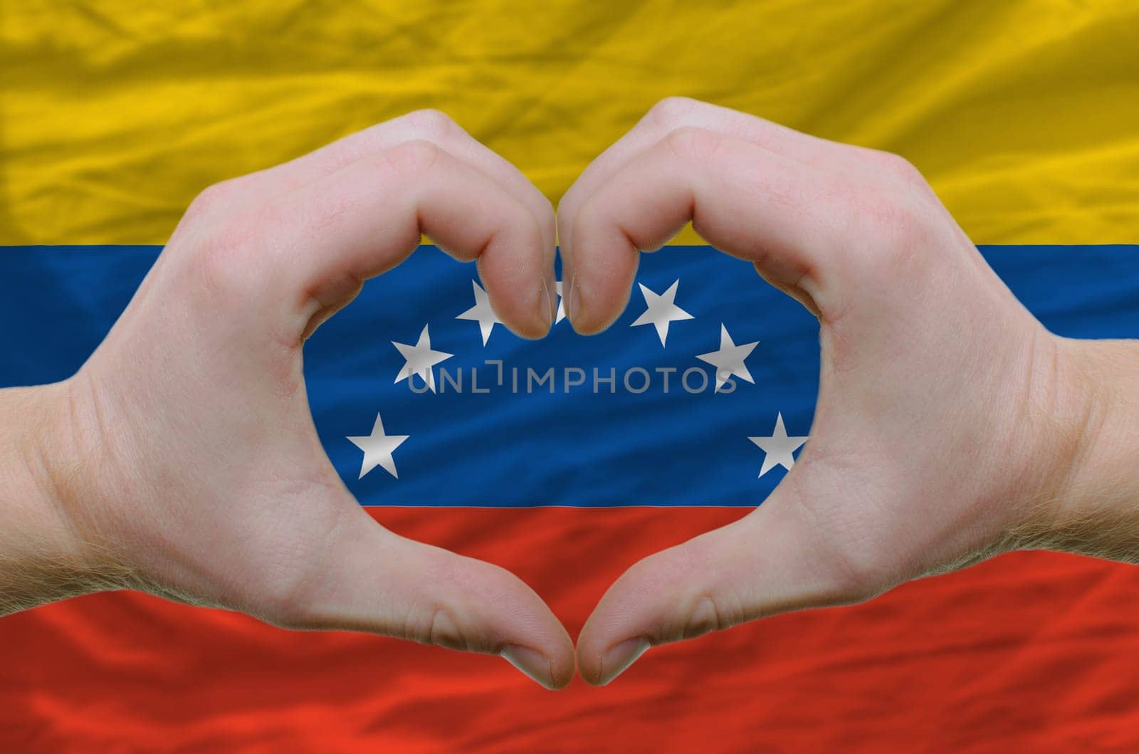 Gesture made by hands showing symbol of heart and love over venezuela flag