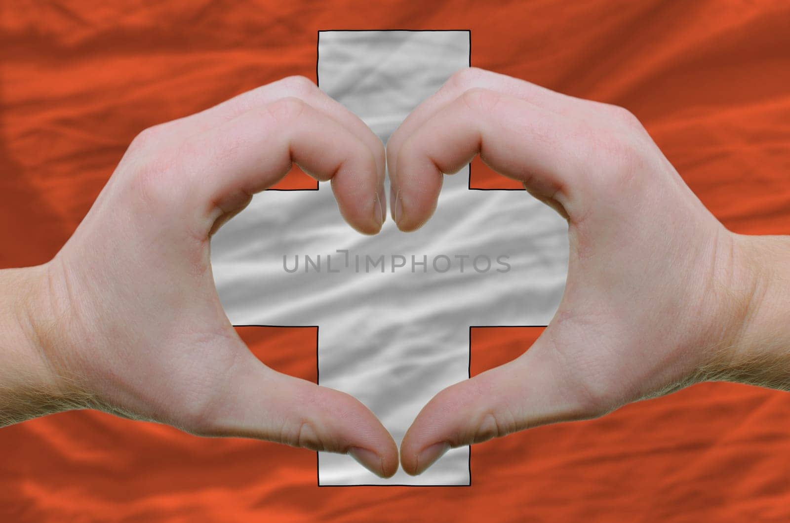 Gesture made by hands showing symbol of heart and love over schwitzerland flag