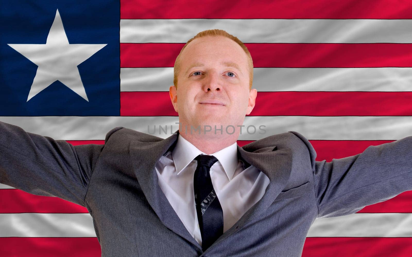 joyful investor spreading arms after good business investment in liberia, in front of flag