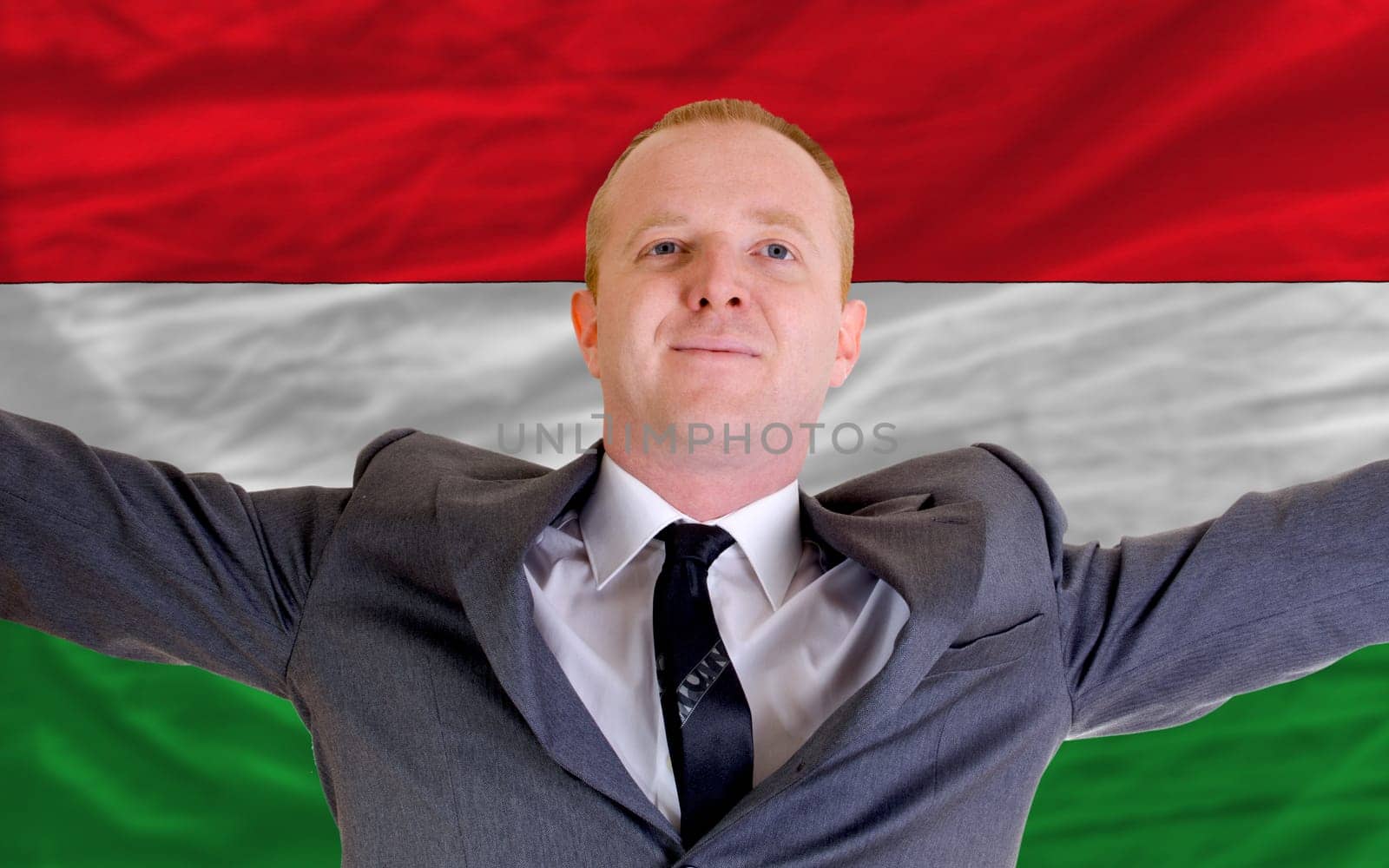 joyful investor spreading arms after good business investment in hungary, in front of flag