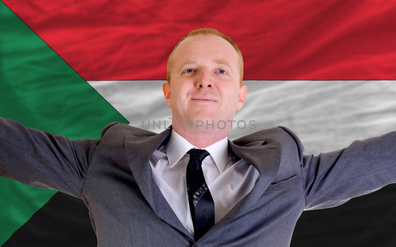 joyful investor spreading arms after good business investment in sudan, in front of flag