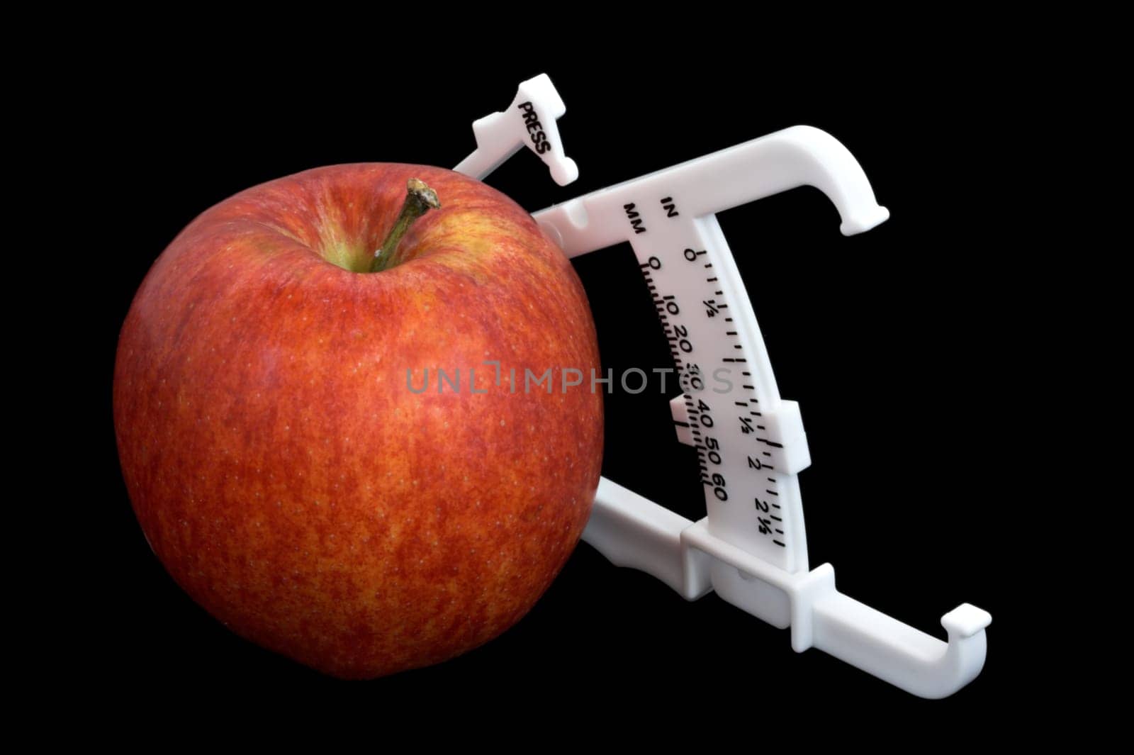 An apple and bodyfat calipers isolated over a black background