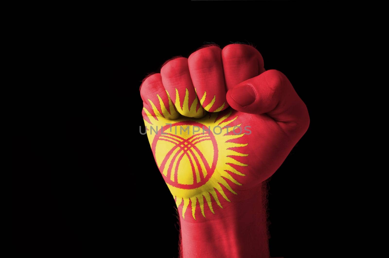 Low key picture of a fist painted in colors of kyrghyzstan flag